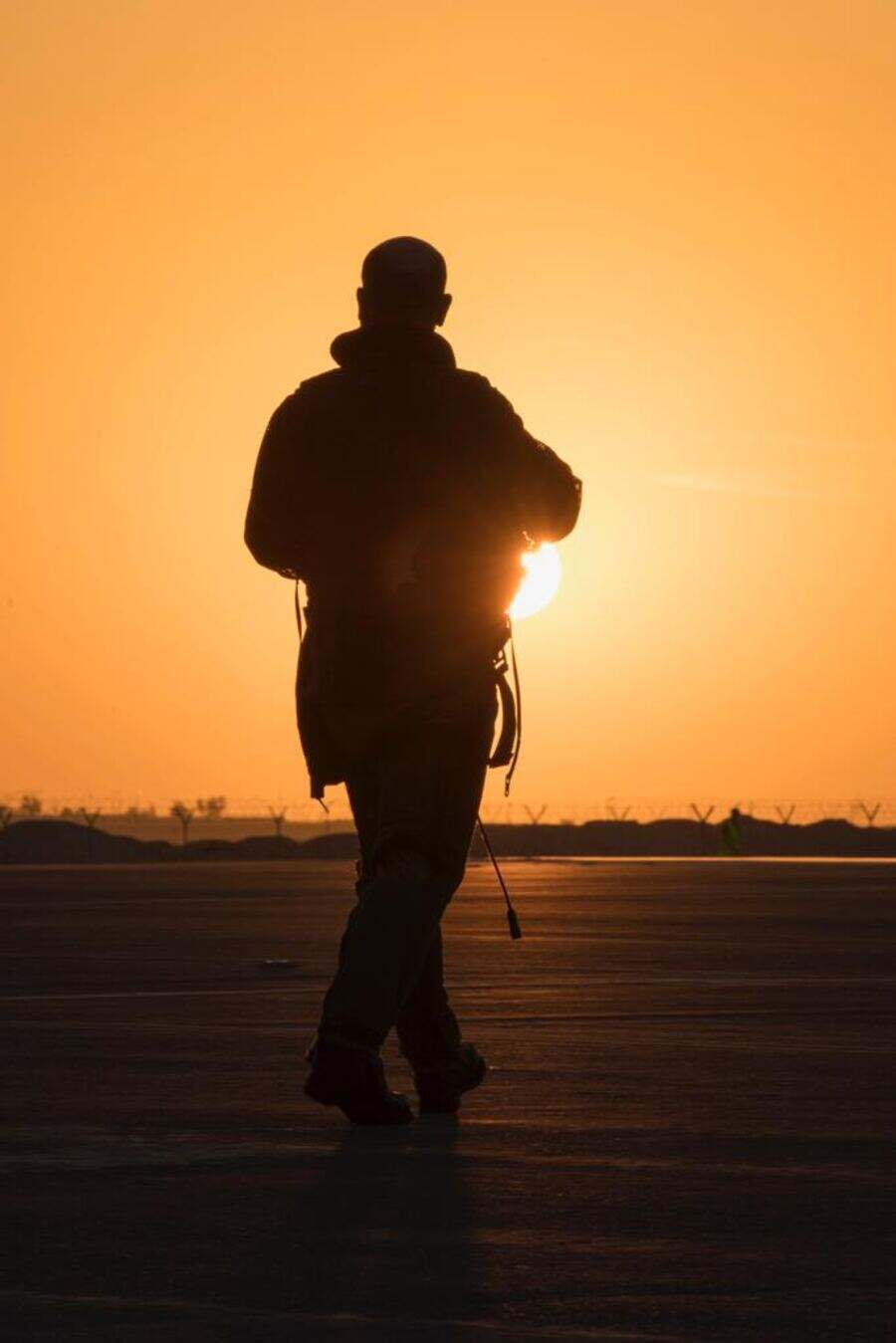 Pilote de chasse marchant vers le soleil couchant sur le tarmac, sac de vol à la main